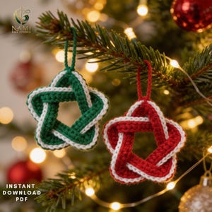 Puede incluir: Dos adornos en forma de estrella de cinco puntas hechos de hilo, uno en verde y blanco y el otro en rojo y blanco. Cada estrella presenta un diseño tejido y anudado con un lazo de hilo a juego en la parte superior. El texto NAMI EMB STUDIO es visible.
