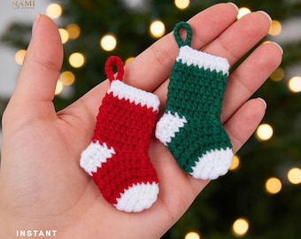 May include: Two miniature crochet stockings, one red and one green, each featuring a white cuff, heel, and toe. Both stockings include a small matching yarn loop at the top for hanging. The text NAMI THE STUDIO and INSTANT DOWNLOAD PDF is visible.