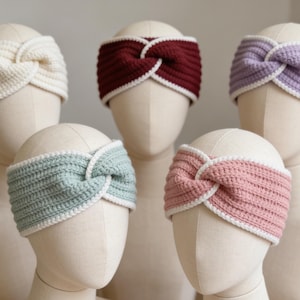 Puede incluir: Una colección de diademas de ganchillo hechas a mano en crema, burdeos, lavanda, verde menta y rosa. Cada diadema presenta un diseño de nudo retorcido y un borde blanco. Las diademas se exhiben en cabezas de maniquí.