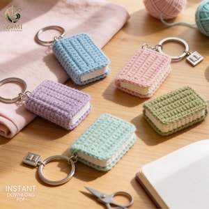 May include: Five crochet book keychains in light blue, pink, lavender, sage green, and mint green. Each keychain features a small rectangular book shape with white pages and a silver metal ring, with some including a small silver book charm.