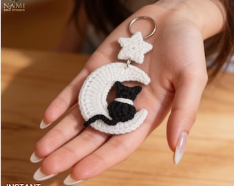May include: A crochet keychain featuring a white crescent moon and a small white star attached to a silver metal ring. A black crocheted cat is positioned on the center of the moon. The item is crafted with white and black yarn in a textured stitch.
