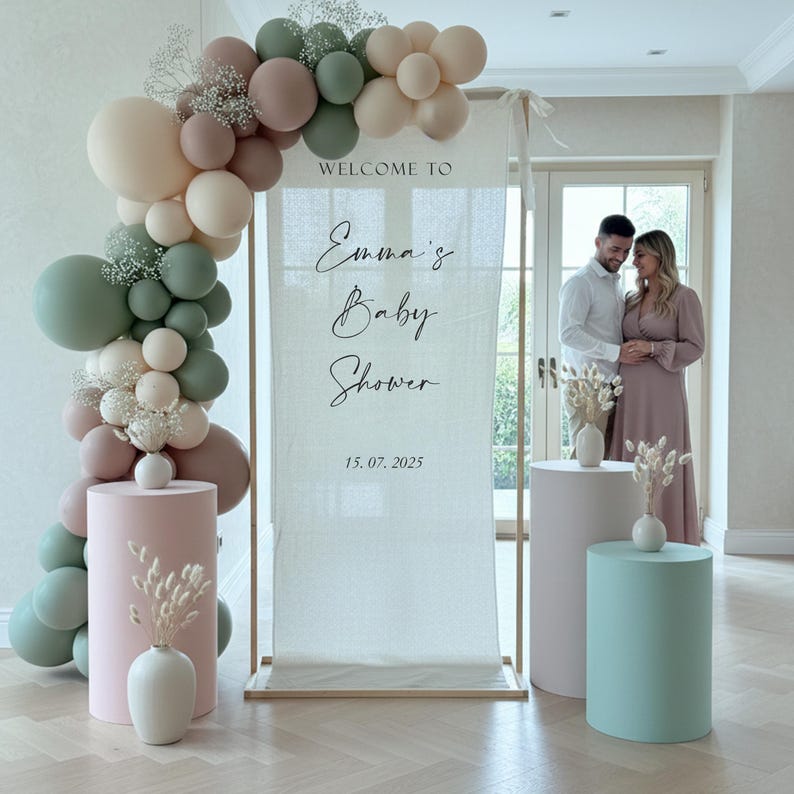Może przedstawiać: Tablica powitalna na baby shower na prostokątnym banerze z tkaniny z łukiem balonowym w kolorze szałwiowej zieleni, beżu i przybrudzonego r&oacute;żu. Baner zawiera napis "WELCOME TO Emma's Baby Shower 15. 07. 2025" i jest prezentowany z cylindrycznymi postumentami.
