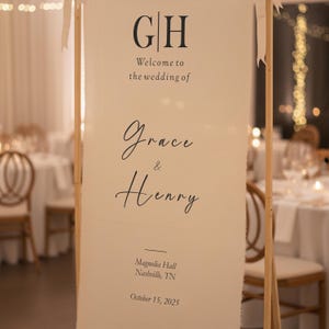 Puede incluir: Un cartel de bienvenida de boda color crema con las iniciales "GH" en la parte superior. El cartel dice "Bienvenida a la boda de Grace & Henry" e incluye el lugar y la fecha: Magnolia Hall, Nashville, TN, 15 de octubre de 2025.