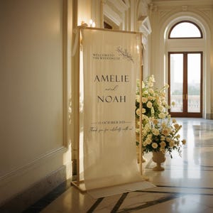 Puede incluir: Un letrero de bienvenida de boda color crema con los nombres "Amelie y Noah" en texto negro. El letrero est&aacute; sobre un marco de madera, con detalles florales y la fecha "15 de octubre de 2025". El letrero est&aacute; en un gran sal&oacute;n con flores.