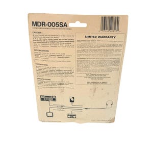 May include: A tan cardboard backing for Sony MDR-005SA stereo headphones. The card features black text including specifications, caution warnings, and a limited warranty. A diagram at the bottom illustrates connection points for the headphones.