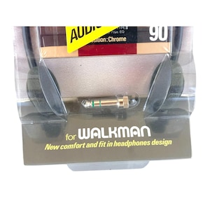 May include: Black foam headphones in clear plastic packaging with a gold-colored audio jack. The packaging features the text "for WALKMAN" and "New comfort and fit in headphones design" along with a yellow label reading "AUDIO" and "90".
