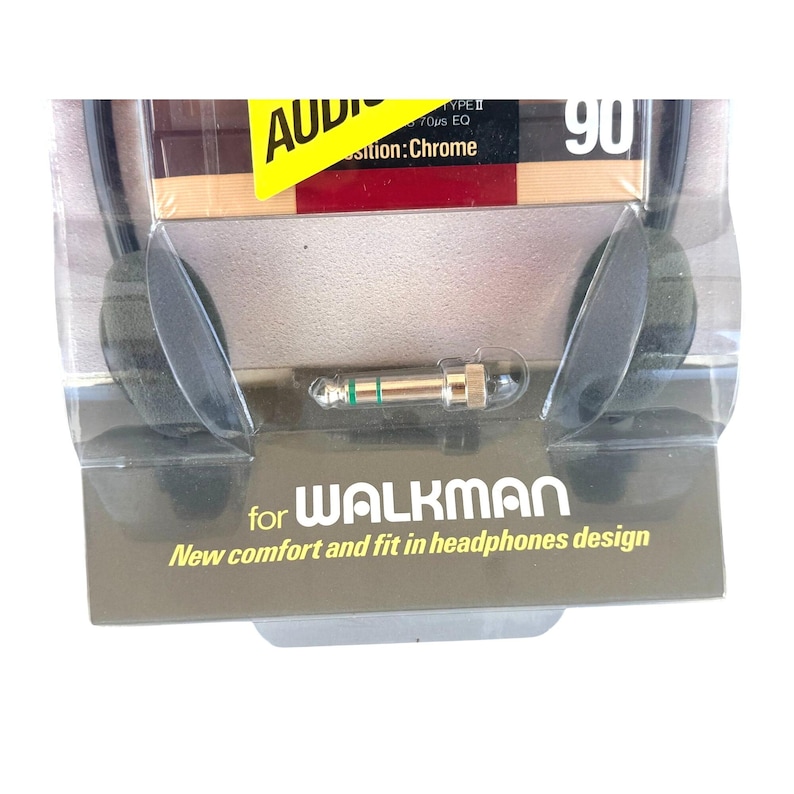 May include: Black foam headphones in clear plastic packaging with a gold-colored audio jack. The packaging features the text "for WALKMAN" and "New comfort and fit in headphones design" along with a yellow label reading "AUDIO" and "90".