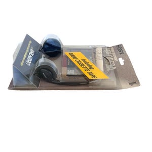 May include: A Sony Walkman stereo headphone set in original blister packaging. The black headphones are visible alongside a 90-minute audio cassette tape. A yellow sticker on the clear plastic cover reads Including AUDIO CASSETTE TAPE.