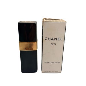 May include: A black Chanel No. 5 spray cologne bottle with a gold band and a matching box. The box is white with black text that reads "CHANEL N&deg;5 SPRAY COLOGNE NET WT. 42.5g."