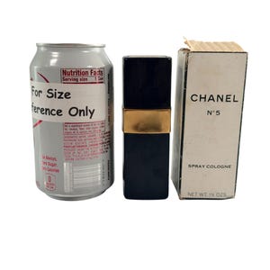 May include: A silver drinks can, a black and gold perfume bottle, and a white box of Chanel No. 5 spray cologne. The box reads "CHANEL N&deg;5 SPRAY COLOGNE NET WT. 1% OZS."