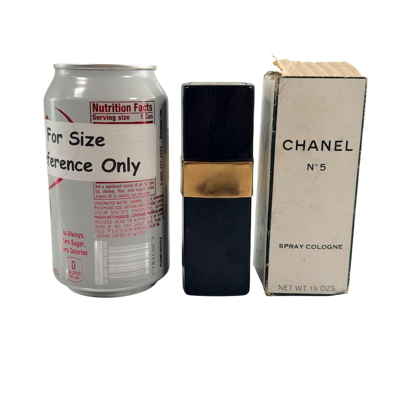 May include: A silver drinks can, a black and gold perfume bottle, and a white box of Chanel No. 5 spray cologne. The box reads "CHANEL N&deg;5 SPRAY COLOGNE NET WT. 1% OZS."