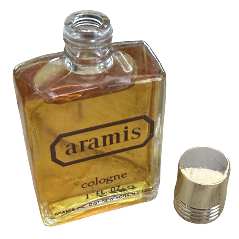 May include: A vintage Aramis cologne bottle with a gold-colored liquid inside. The bottle is rectangular with a clear glass top and a gold cap. The label reads "aramis cologne 1 FL. OZ."
