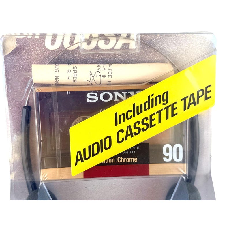 May include: A Sony brand audio cassette tape in a clear plastic blister pack. The tape is labeled as Type II Chrome 90. A bright yellow diagonal sticker across the front reads Including AUDIO CASSETTE TAPE. A white paper insert is visible above.