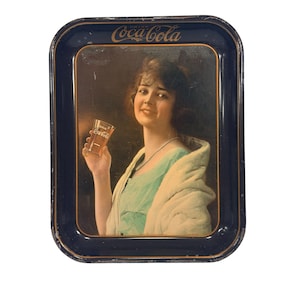 Puede incluir: Bandeja de servicio vintage de Coca-Cola con borde azul oscuro e imagen de una mujer sosteniendo un vaso de Coca-Cola. La bandeja presenta el logotipo de Coca-Cola en la parte superior y es un artículo de colección.
