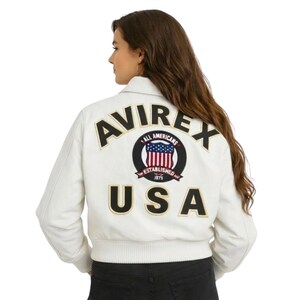 May include: A white ceramic mug with a black handle and the text "But First, Coffee" in a bold, black font. The mug is set against a blurred background, suggesting a cozy setting.