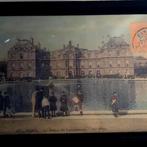 May include: Vintage postcard of the Palais du Luxembourg in Paris, France, featuring a large building with a pond in front. The postcard has a faded appearance, with people visible near the pond. A stamp is in the upper right corner.