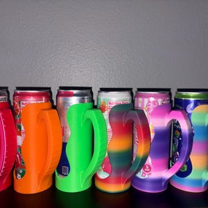 May include: A row of six plastic can holders with ergonomic handles, each featuring a distinct color or pattern. The holders are shown in solid pink, orange, and neon green, followed by three multi-colored gradient designs in rainbow hues.