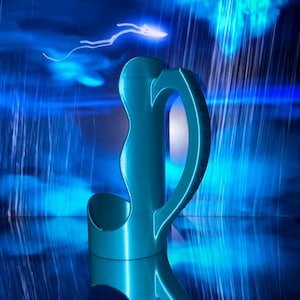 May include: A teal-colored 3D printed cup holder with a smooth, curved vertical handle and a cylindrical base. The object features a distinct wave-like silhouette along the side and is captured with a reflective surface finish.