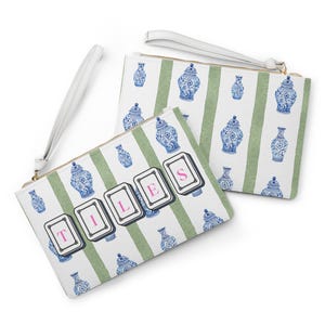 May include: Two white clutch bags with a green striped pattern and blue and white vase illustrations. One bag has the word "TILES" spelled out with pink letters on playing card-like shapes. Both bags have a white wrist strap.