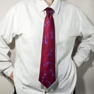 May include: A burgundy tie with a repeating pattern of purple ants. The tie is worn over a white button-down shirt. The ants are detailed with visible legs and antennae.