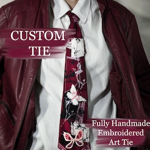 Op de afbeelding: Een op maat gemaakte bordeauxrode stropdas met geborduurde vlinder- en bloemmotieven. De stropdas heeft een wit en zwart patch en een roze kanten rand. De tekst "CUSTOM TIE" en "Fully Handmade Embroidered Art Tie" zijn zichtbaar.
