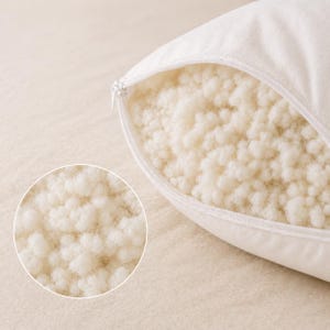 May include: A white pillow with a zippered opening revealing a filling of small, off-white, textured, cloud-like clusters. A circular inset shows a magnified view of the dense, granular, and soft material inside the pillow casing.