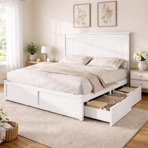 Peut inclure: Un lit en bois blanc avec une tête de lit à lattes et deux tiroirs coulissants. Le lit est fait avec de la literie blanche et des oreillers décoratifs. La pièce a une palette de couleurs neutres avec un tapis beige et deux tableaux encadrés.