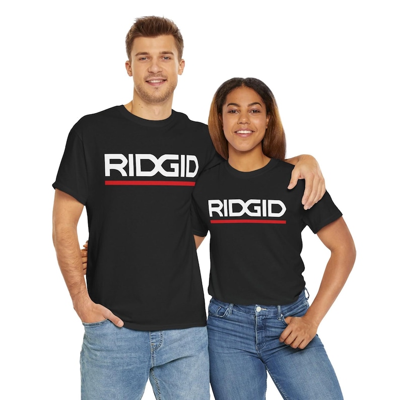 Puede incluir: Dos personas vestidas con camisetas negras con la palabra "RIDGID" en letras blancas en bloque sobre una l&iacute;nea horizontal roja. Las camisetas se combinan con vaqueros azules. El fondo es blanco liso.