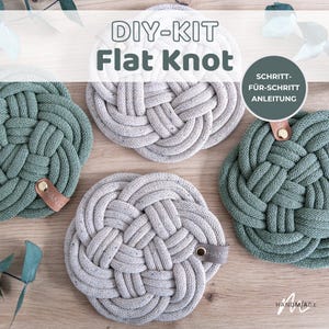 Könnte beinhalten: Ein DIY-Set für flache Knoten-Untersetzer aus beigefarbenem und salbeigrünem geflochtenem Seil. Jeder Untersetzer hat ein kleines lederartiges Etikett mit einer goldenen Niete. Der Text lautet DIY-KIT Flat Knot und SCHRITT-FÜR-SCHRITT ANLEITUNG.