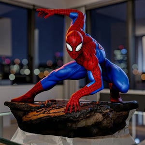 May include: A detailed statue of Spider-Man in a dynamic pose, wearing his iconic red and blue suit. The figure is crouched on a rocky base, with one arm outstretched. The background shows a cityscape at night.