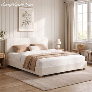 May include: A cream-colored upholstered bed with a tall headboard, adorned with pillows and a brown throw blanket. The room features a framed botanical print, a bedside table with a lamp, and a neutral-toned rug, creating a serene bedroom setting.
