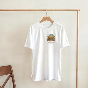 Könnte beinhalten: Weißes T-Shirt mit einer kleinen Grafik auf der Vorderseite. Die Grafik zeigt ein Sonnenuntergangsdesign mit den Worten "Team Passport" und "We make our own Adventure" in Grün, Orange und Braun.