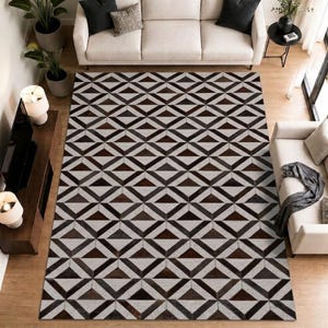 May include: A rectangular area rug featuring a repeating geometric pattern of dark brown and light grey triangles arranged in a diamond grid layout. The rug covers the floor space between two light-coloured sofas and a wooden media console.
