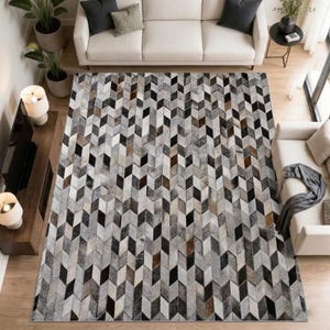 Puede incluir: Una alfombra rectangular con un patrón geométrico de espiga compuesto por baldosas individuales en tonos negro, blanco, gris y marrón. La alfombra muestra un efecto de cubo tridimensional repetitivo en toda su superficie.