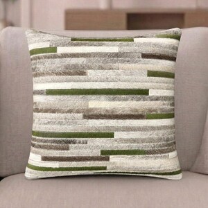 May include: A square throw pillow featuring a patchwork design of horizontal strips in shades of forest green, cream, and various tones of grey and brown. The surface has a textured, hair-on-hide appearance with visible stitching between each strip.