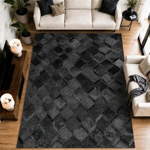 Puede incluir: Una alfombra rectangular grande con un patrón geométrico de cubos repetidos en gris oscuro y negro. La alfombra tiene una superficie texturizada con varios tonos de gris y negro, creando un efecto visual tridimensional sobre el suelo.