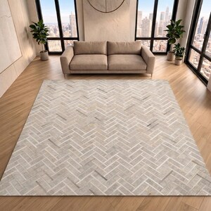May include: A rectangular rug with a herringbone pattern in beige, grey, and white. The rug is on a wooden floor in a room with a beige sofa and large windows overlooking a city. The rug's dimensions are in centimetres.