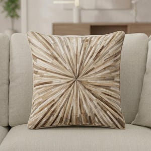 May include: Square decorative pillow with a radial pattern in shades of brown and beige. The pillow is made of a patchwork of rectangular pieces, creating a sunburst design. The pillow is placed on a light beige sofa.