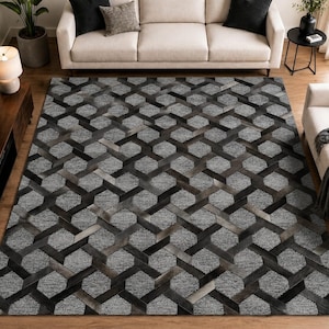 Puede incluir: Una alfombra rectangular con un patrón geométrico repetitivo de hexágonos entrelazados en tonos gris carbón, gris pizarra y negro. El diseño crea un efecto visual tridimensional con segmentos grises texturizados y líneas negras suaves.