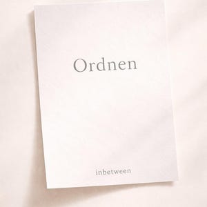 Può includere: Una carta bianca con la parola "Ordnen" in lettere grigie in alto e la parola "inbetween" in basso. La carta è leggermente angolata, con ombre morbide.