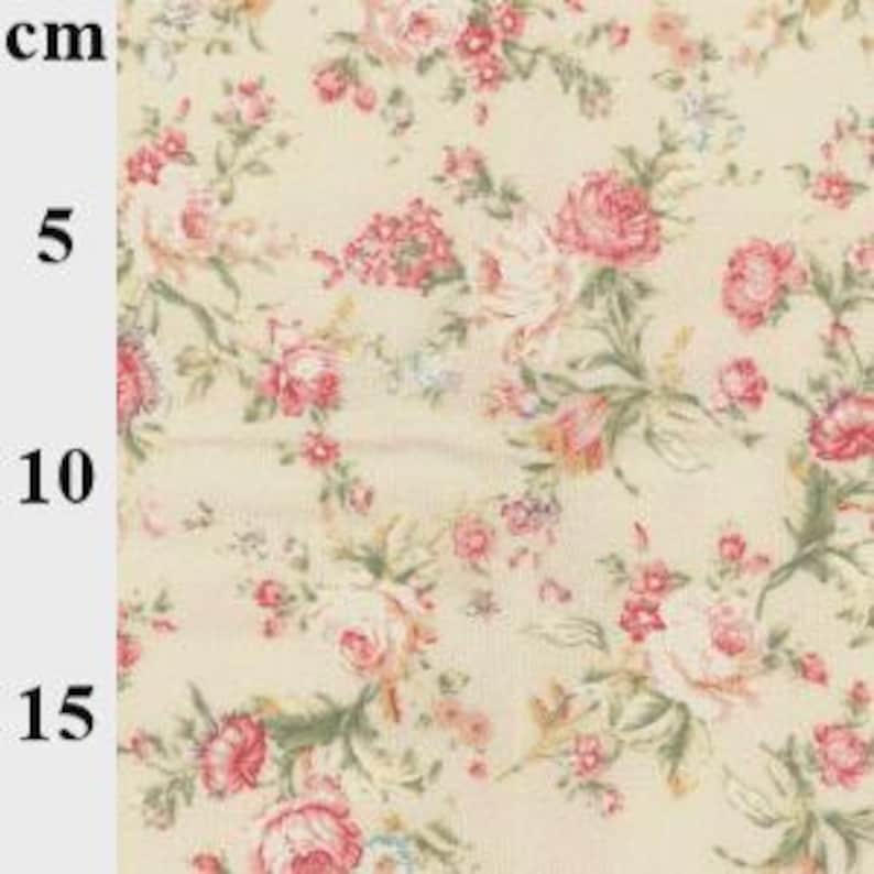 May include: Close-up of a floral fabric with a cream background. The fabric features a pattern of pink and red roses with green leaves. Measurements in centimeters are visible on the left side of the image.