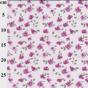 May include: Floral fabric with a repeating pattern of purple and white flowers and green stems on a light pink background. The fabric is marked with a centimeter ruler along the left edge.