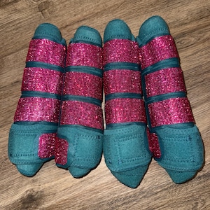 Peut inclure: Un ensemble de quatre bandes de repos pour chevaux de couleur sarcelle, dotées de trois sangles horizontales recouvertes de strass rose vif étincelants. Chaque bande est faite d'un tissu sarcelle uni avec des coutures assorties et des fermetures auto-agrippantes.