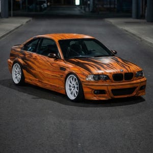 May include: An orange coupe with a wood grain design, white wheels, and black accents is parked on a dark road. The car's body has a unique pattern, and the headlights are visible.