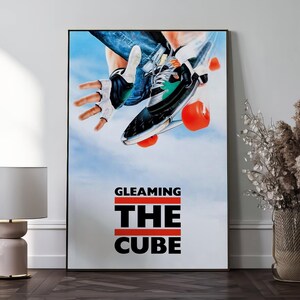 Op de afbeelding: Een ingelijste poster met een skateboarder in actie, met een zwart-witte sneaker en oranje wielen. De poster heeft een blauwe luchtachtergrond en de tekst "GLEAMING THE CUBE" in vette zwarte letters met rode lijnen.