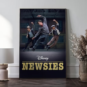 Puede incluir: Un póster enmarcado de la película musical de Disney "Newsies". El póster muestra a tres jóvenes en poses dinámicas, ambientados en una calle de la ciudad. El título "Newsies" se muestra en letras doradas.