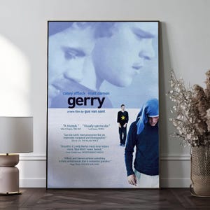 Puede incluir: Un póster enmarcado de la película "Gerry" con Casey Affleck y Matt Damon. El póster tiene una combinación de colores azul y blanco con el título y los créditos de la película. Una persona con una capucha azul está en primer plano.