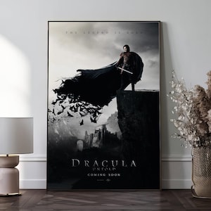 Puede incluir: Póster enmarcado de la película "Dracula Untold". La imagen muestra una figura con capa sobre un acantilado, sosteniendo una espada, con murciélagos volando. El texto "THE LEGEND IS BORN" está arriba, con "DRACULA UNTOLD" y "COMING SOON" debajo.
