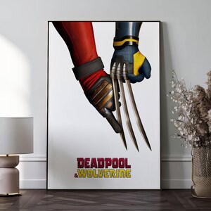 K&ouml;nnte beinhalten: Gerahmtes Poster mit einer Nahaufnahme von zwei Superhelden-H&auml;nden. Eine Hand ist in einem roten Anzug mit schwarzem Armband und goldenen Akzenten, die andere in einem blau-gelben Anzug. Das Poster tr&auml;gt die Worte "DEADPOOL & WOLVERINE" in Rot und Gelb.