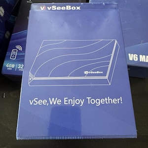 May include: A blue vSeeBox box with a white outline of a device and the text "vSee, We Enjoy Together!". Other boxes are visible in the background, suggesting a tech product.